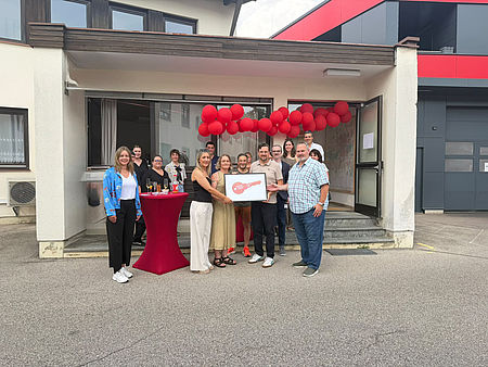 Eröffnung ambulante Pflege Dieses Bild zeigt mehrere Personen, die vor einem Eingang mit rot geschmückten Luftballons stehen. In den Händen halten sie ein Bild, auf dem ein goldener Schlüssel abgebildet ist.