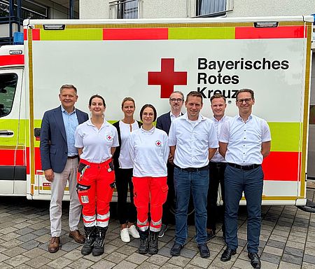 Ausschreibung Rettungsdienst Dieses Bild zeigt mehrere Personen die nebeneinander vor einem Rettungswagen stehen.